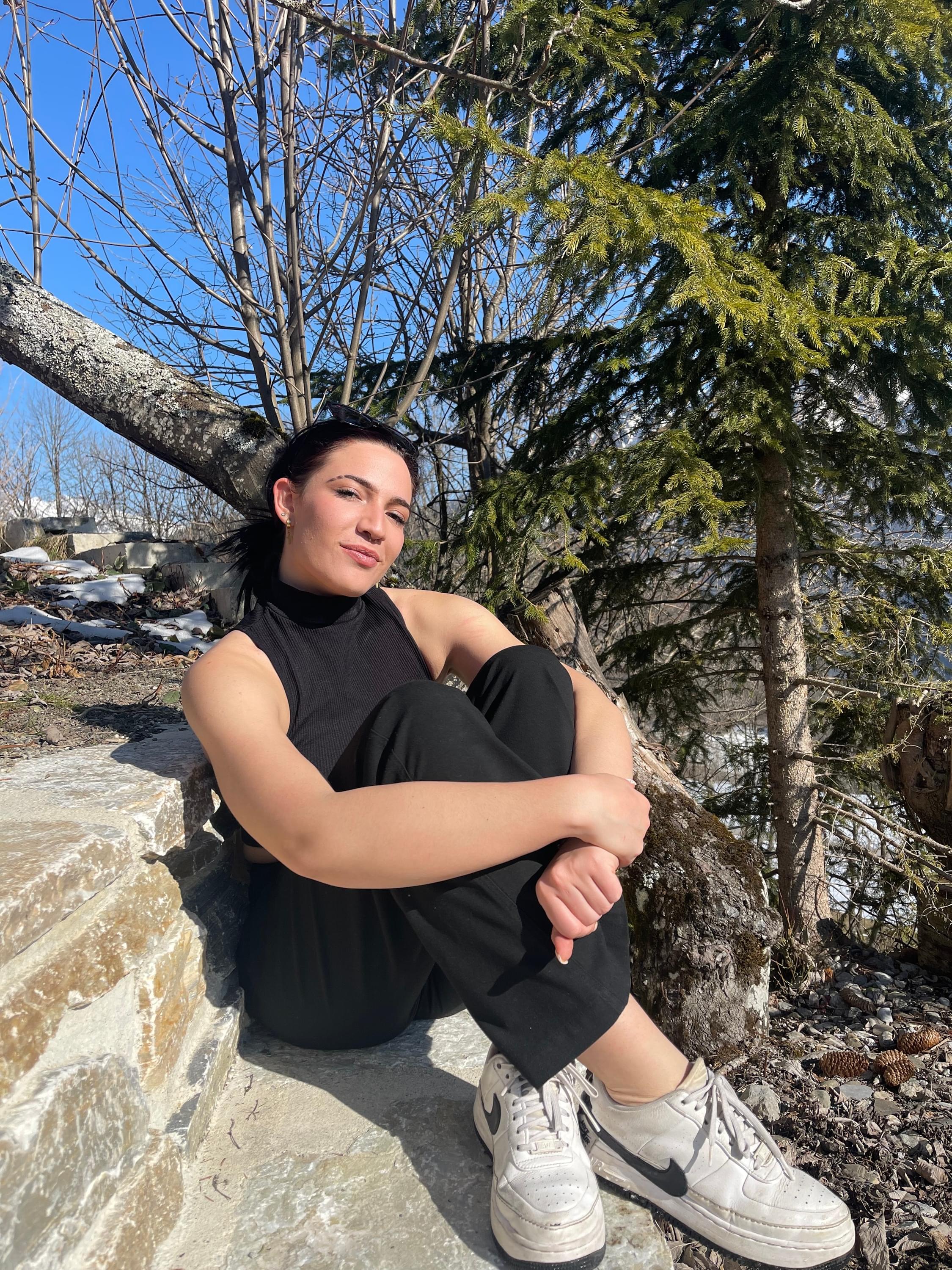 Woman sitting on a tree branch, mountains, outdoor, sunglasses, sunlight, sky